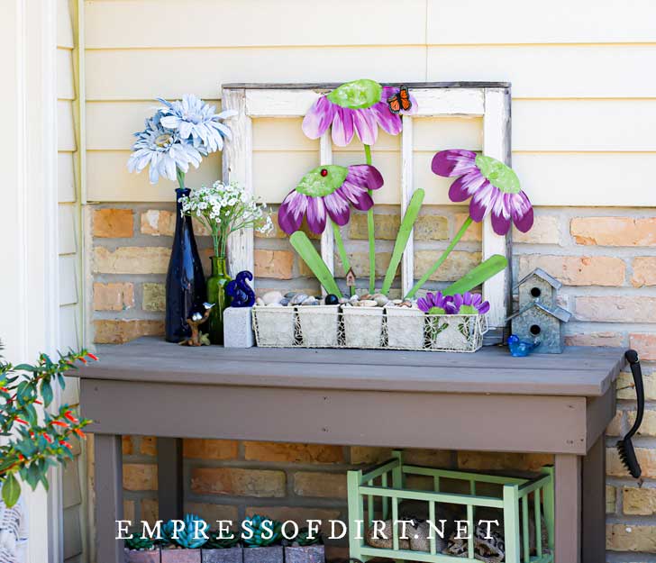 Gray table-style potting bench with decorative, metal garden art flowers.